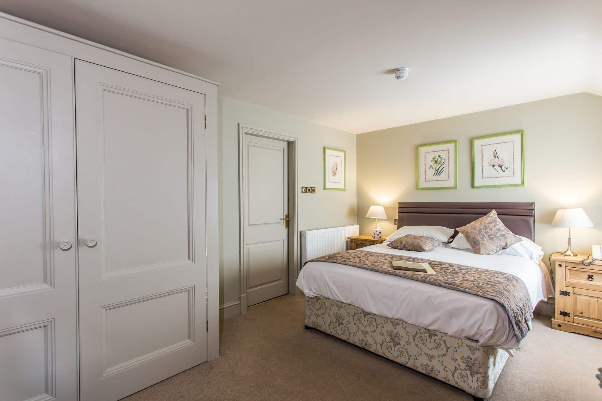 A bright double room with painted panelled wardrobes and botanical prints