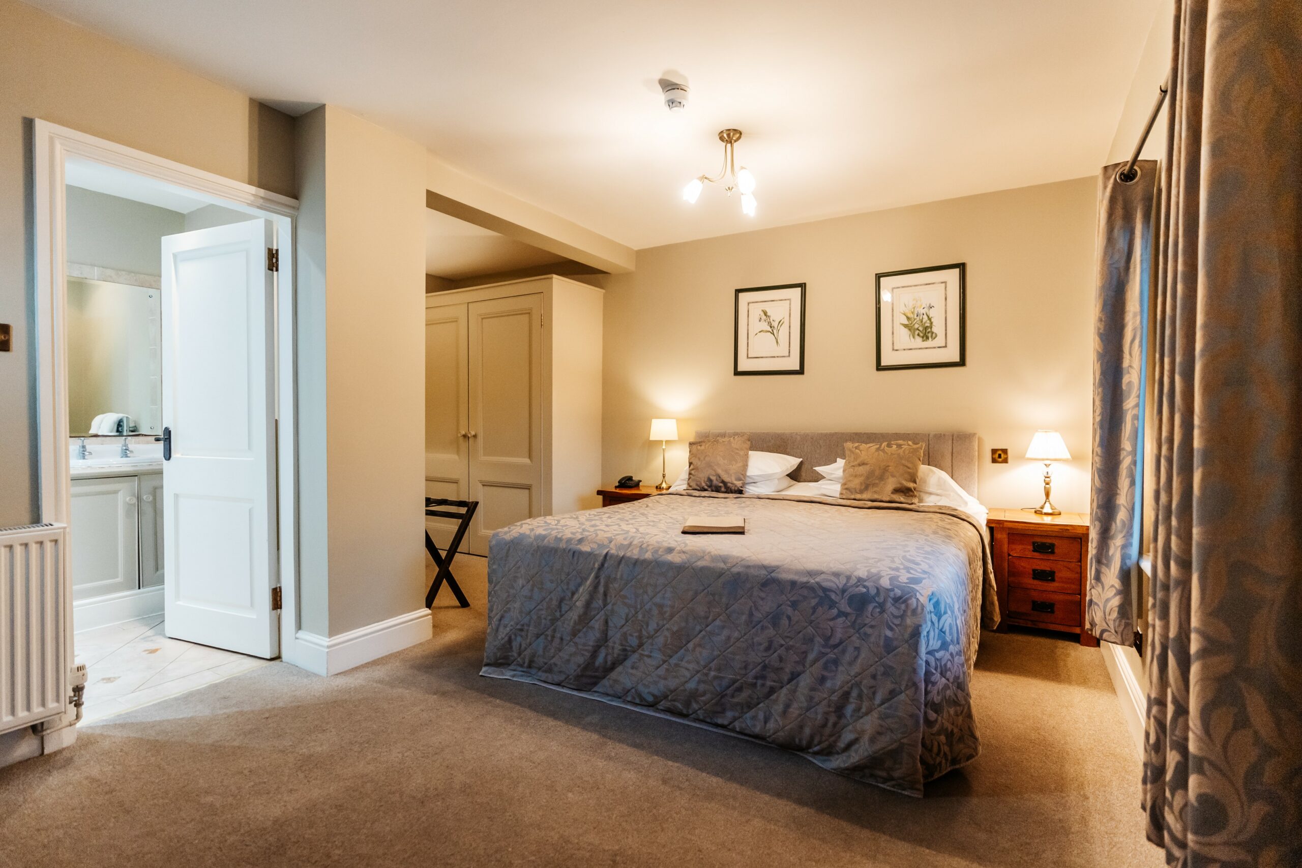 A double bedroom with a grey quilted bedspread, bedside lamps and an en suite bathroom